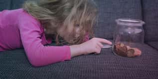 Child lying on a couch, pointing at coins in a jar