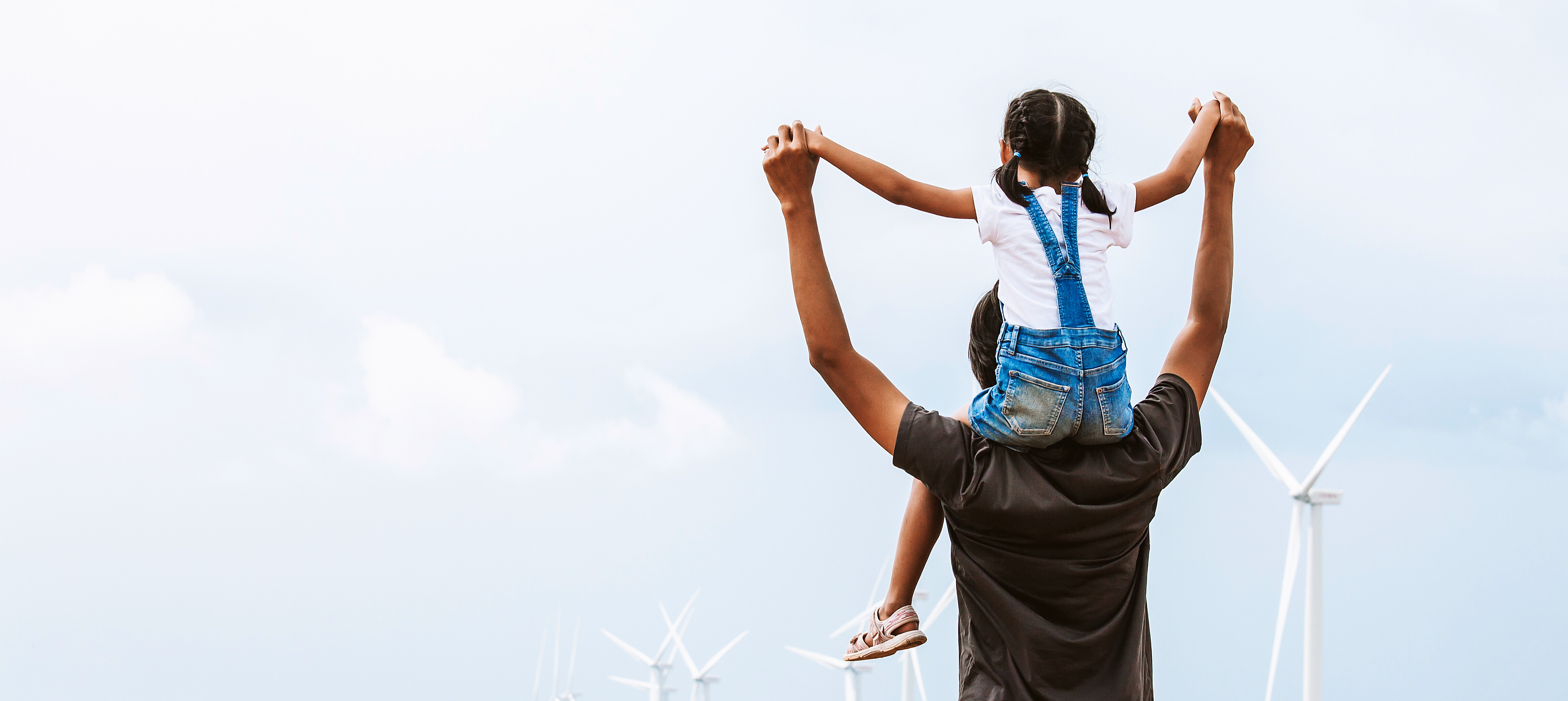 Adult lifting a child on their shoulders near wind turbines