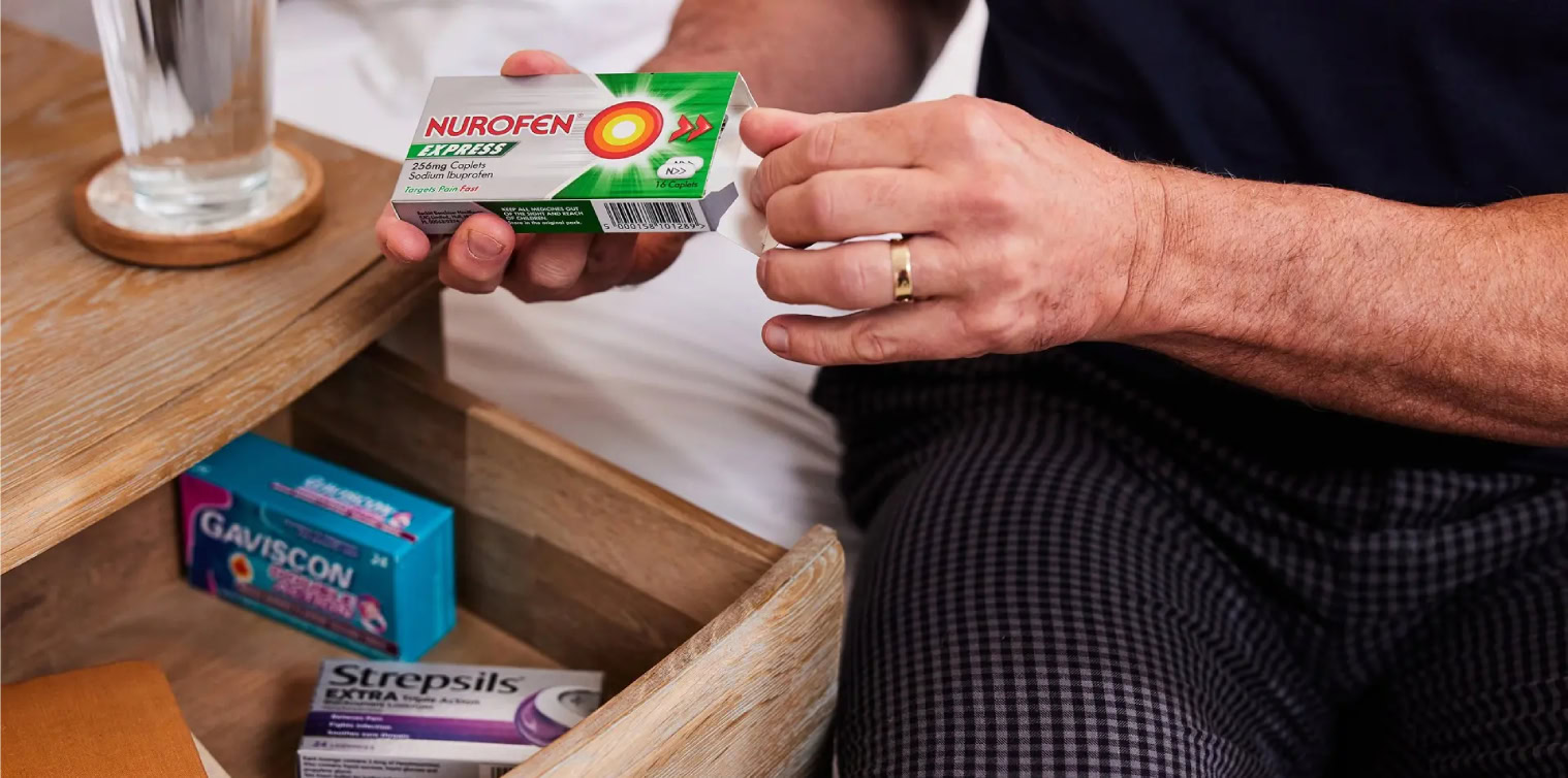 Person opening a box of Nurofen medicine beside an open drawer with other medications.