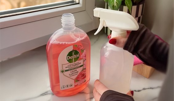bottle of pink Dettol concentrated multi-purpose cleaner next to a clear spray bottle being held by a person with red nail polish.