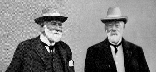 Black-and-white portrait of two older men wearing hats and formal attire.