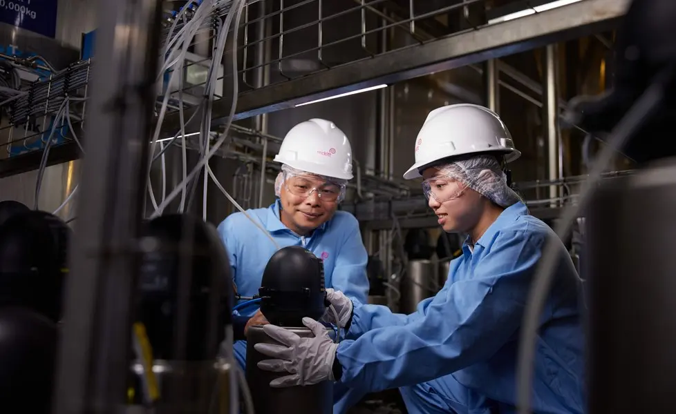 Two factory workers in safety gear inspecting industrial equipment.