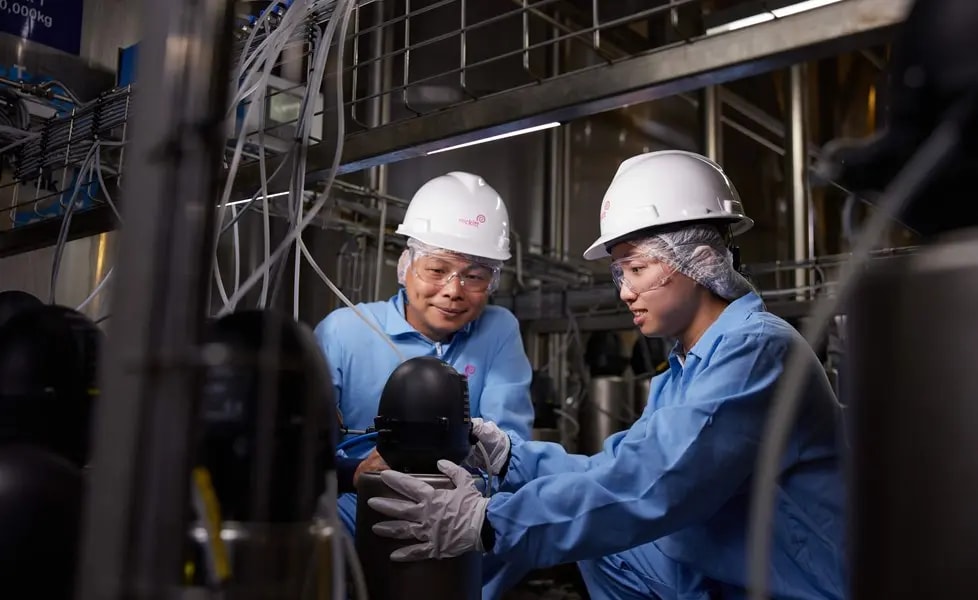 Two factory workers in safety gear inspecting industrial equipment.