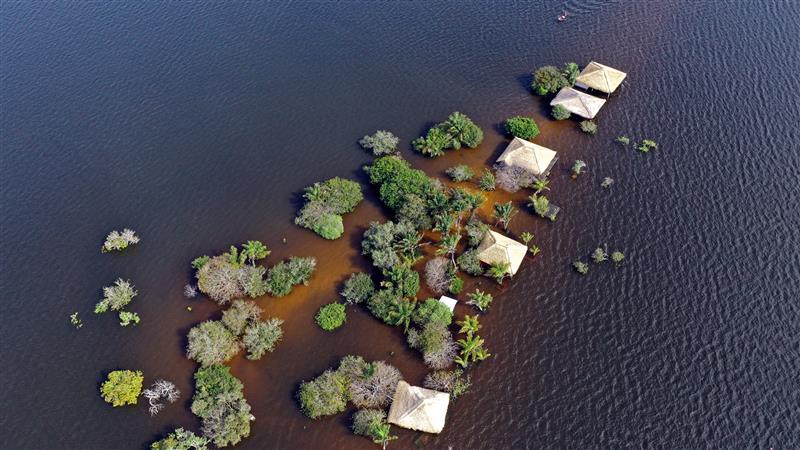 Aerial view of flooded land with trees and small huts partially submerged
