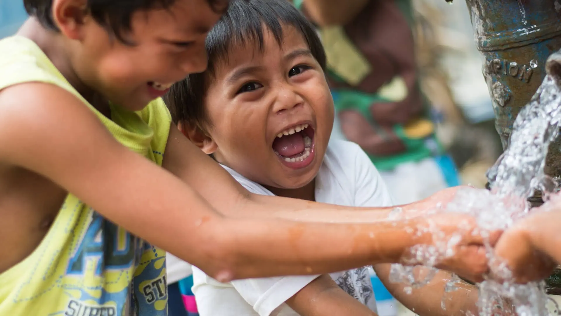 Children laughing and playing with water at an outdoor tap