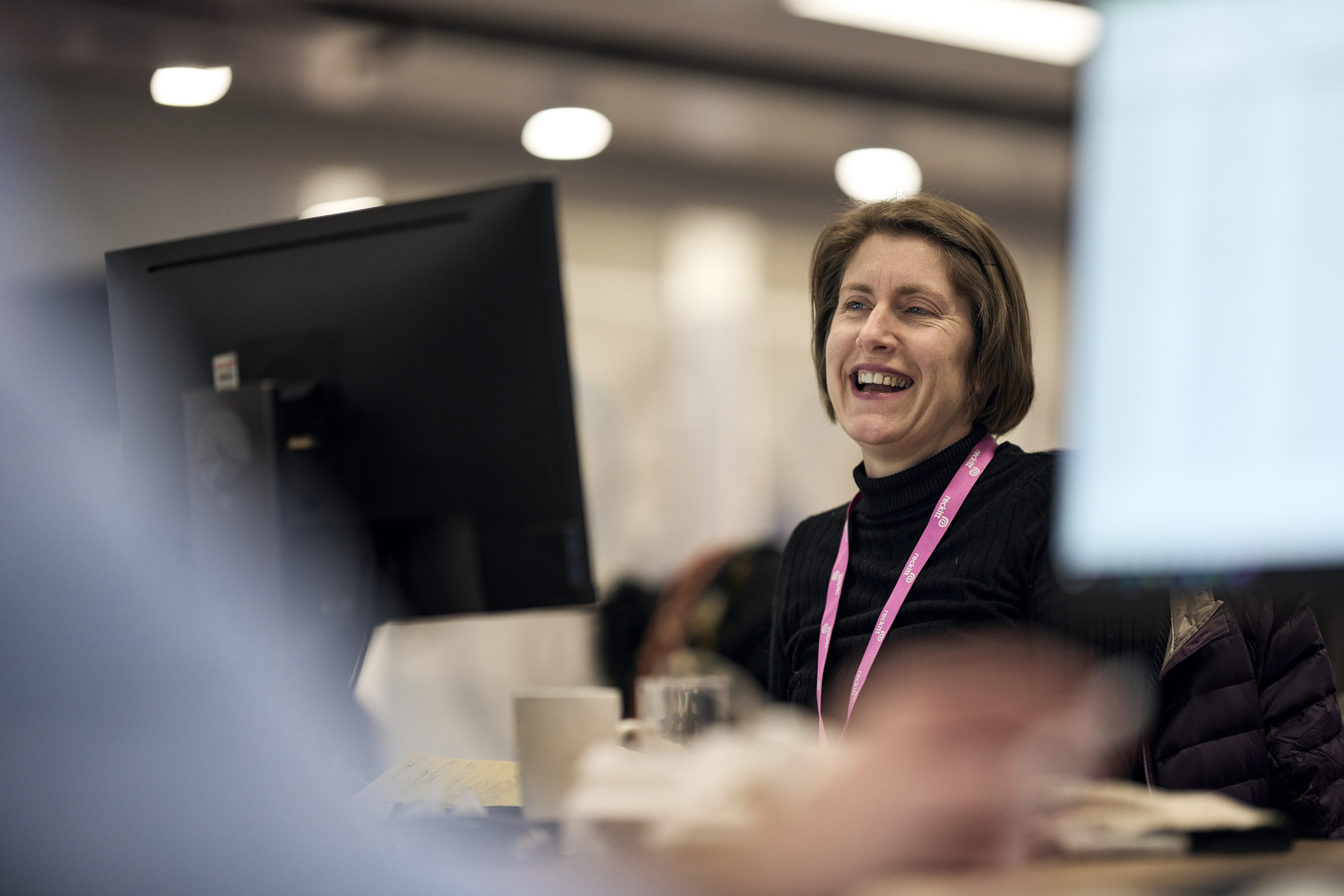 Employee smiling while working at a computer in an office environment with a company lanyard visible