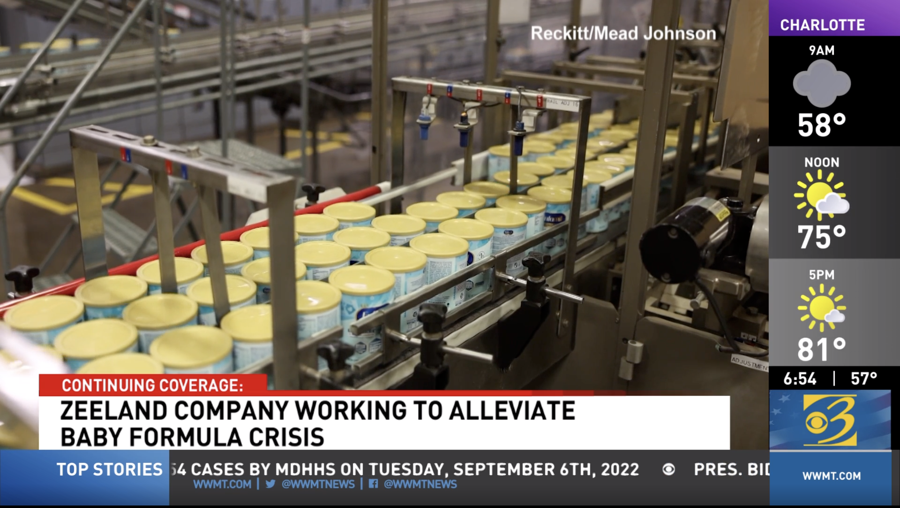 News screenshot showing infant formula cans moving through a manufacturing production line during coverage of the baby formula shortage