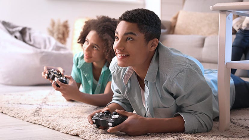 Two children play video games together while lying on front of the TV.