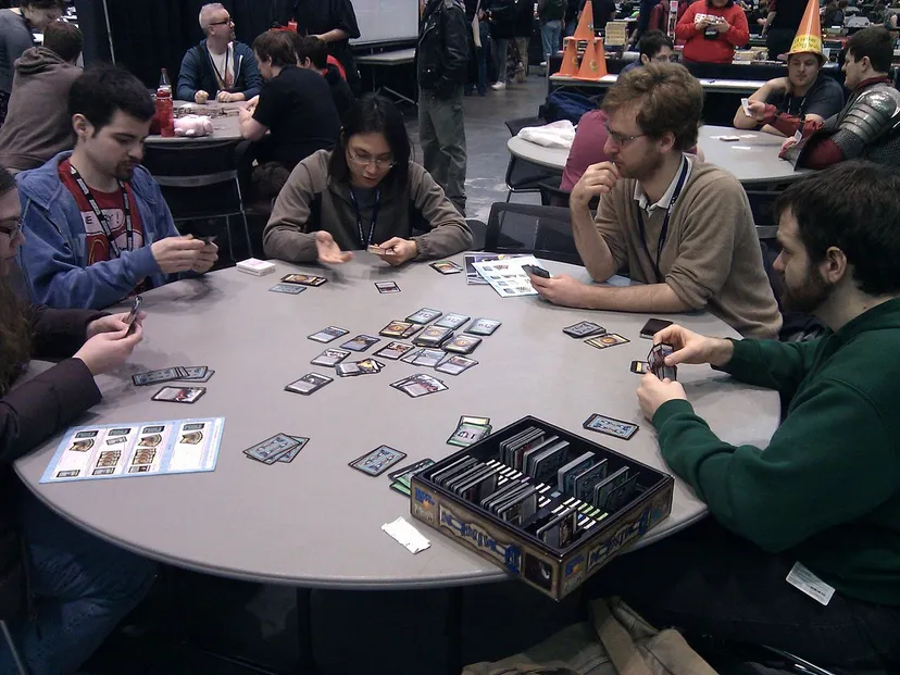 Four players gather around a table to play the card game Dominion.