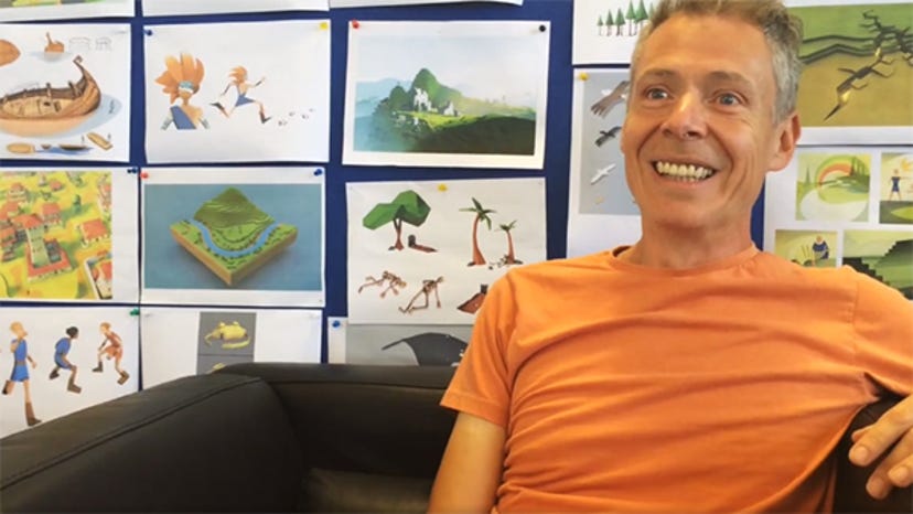 Paul Mclaughlin smiles while sitting in front of art assets for Godus