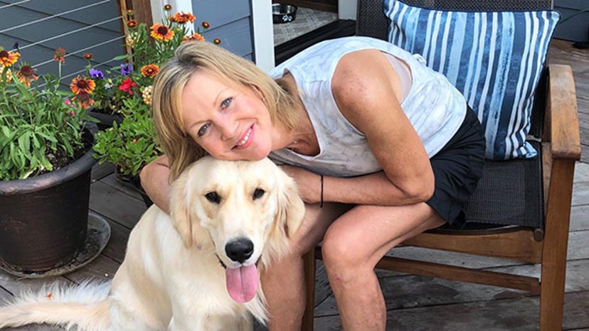 A photograph of Cherie Lutz. She is hugging her golden retriever while sitting on her front porch.