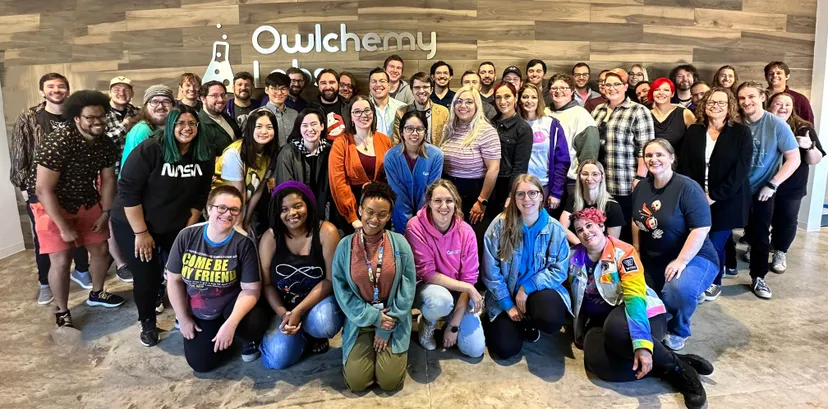 A group photo of the Owlchemy Labs employees gathered in front of the company sign.