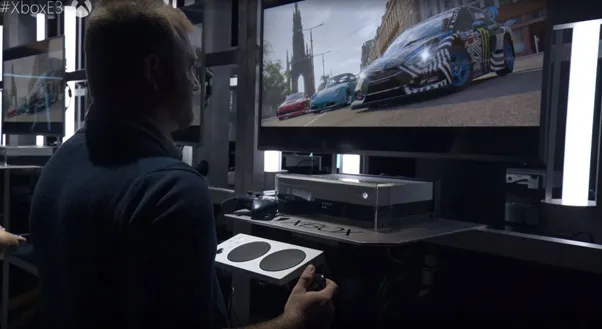 Solomon playing Forza on a large screen, using a one-handed controller plugged into an xbox adaptive controller
