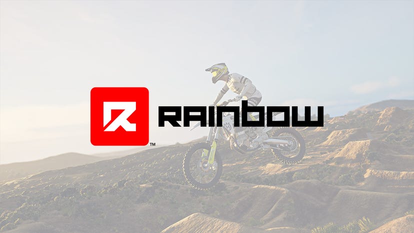 The Rainbow Logo overlaid on a screenshot from MX vs ATV Legends showing a dirt bike mid-jump