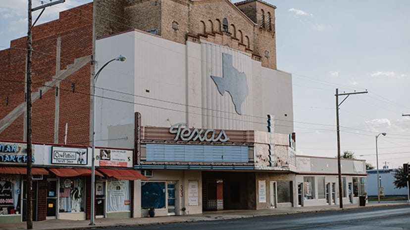 A photograph of a Texas movie theater. The word "Texas" is on the marquee