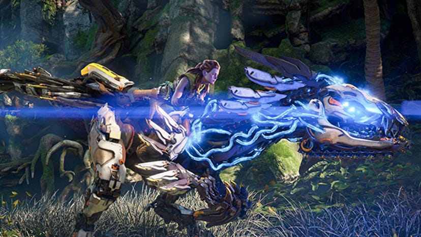 A screenshot from Horizon Forbidden West. Protagonist Aloy rides a mechanical dinosaur that's glowing with blue light.
