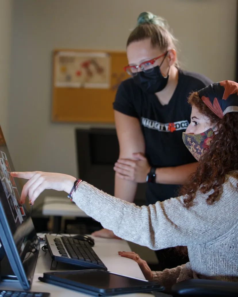 A picture showing two people, one pointing at something on a digital screen while the other looks on to offer advice.