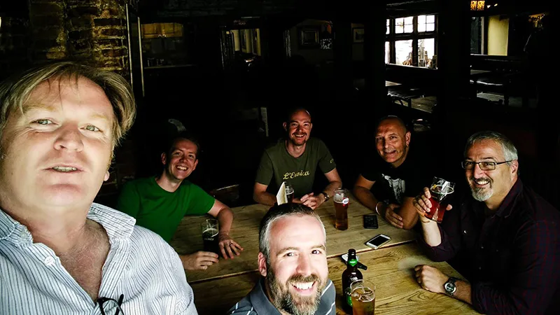 The Two Point Studios team gathers on their first day in a pub. Mark holds the camera in a selfie shot, Gary drinks a beer on the far right.