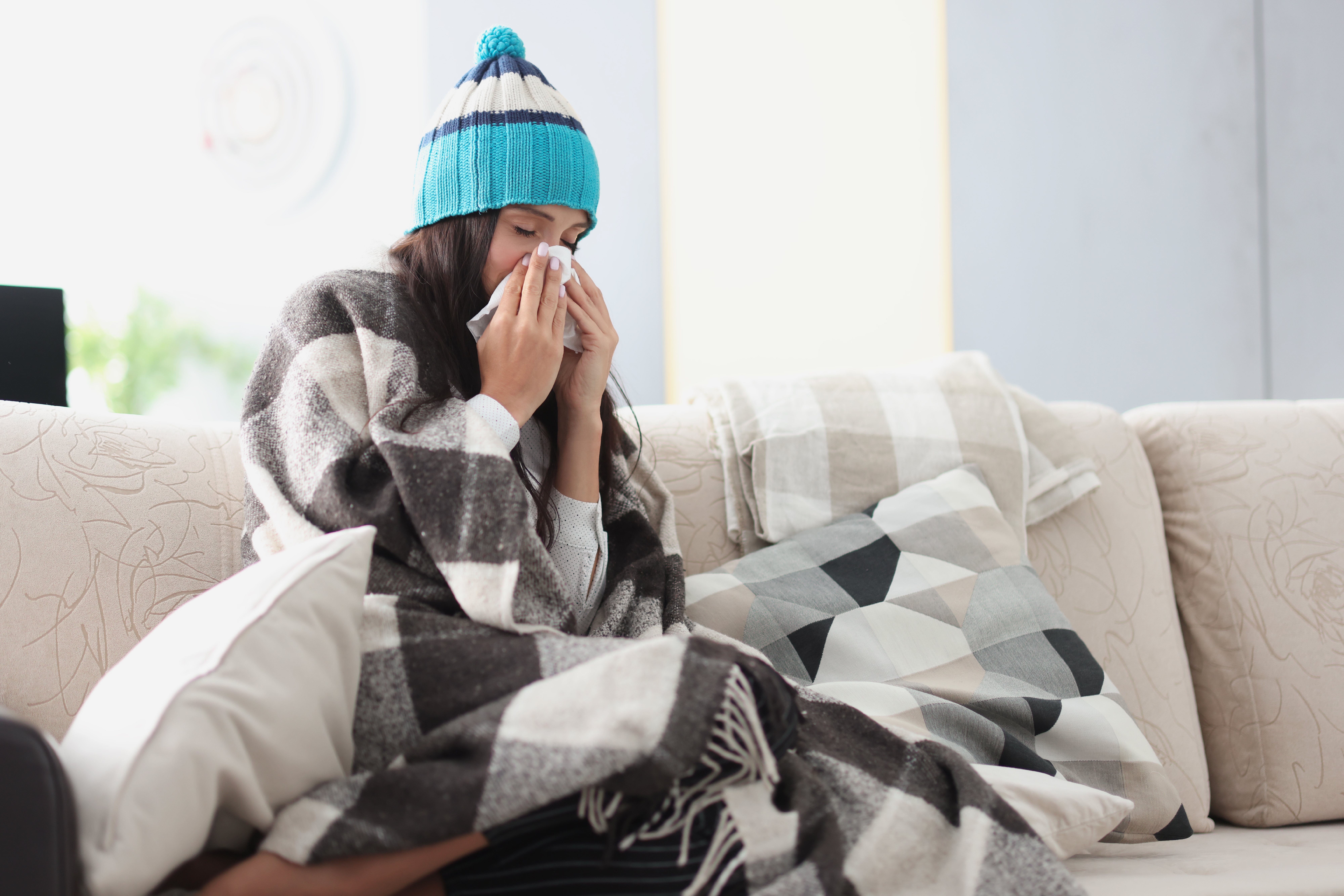 Sick woman with flu cleaning nose with tissue on sofa.