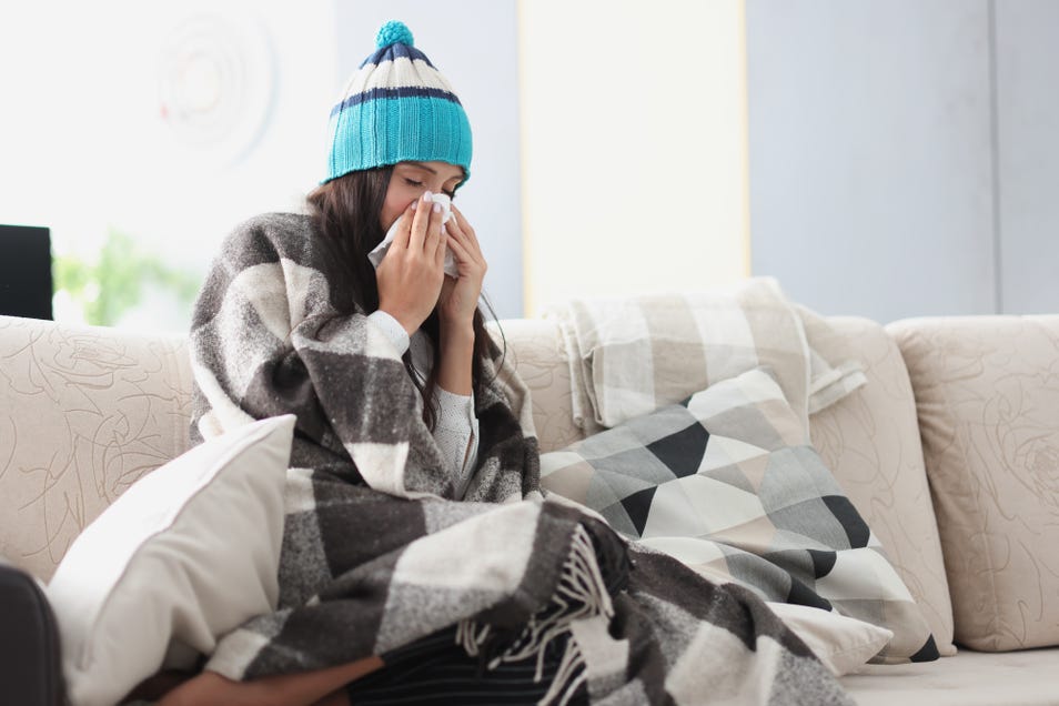 Sick woman with flu cleaning nose with tissue on sofa.