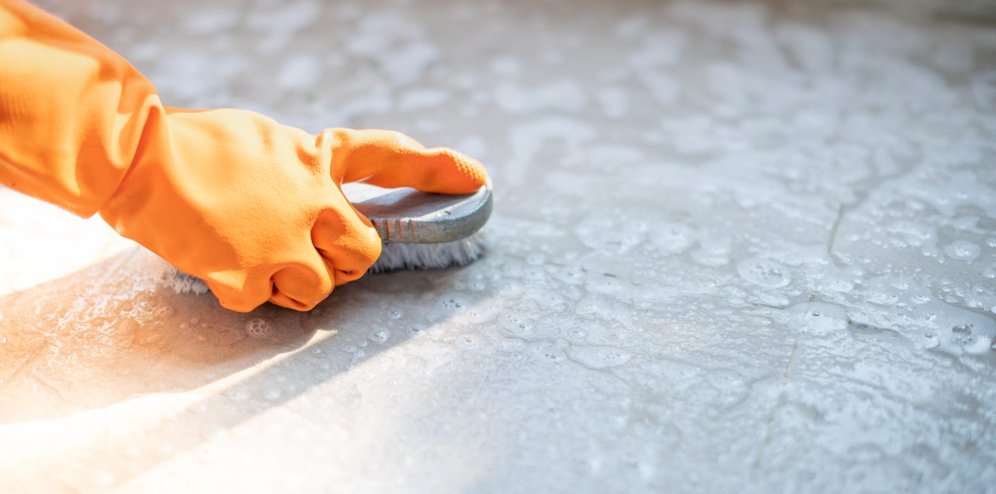 A person wearing a glove and cleaning the concrete floor with a brush