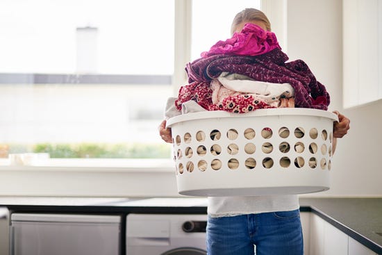 A woman carrying a basket filled with a large pile of clothes