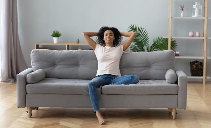 Présente une femme dans son salon qui relax sur son sofa.