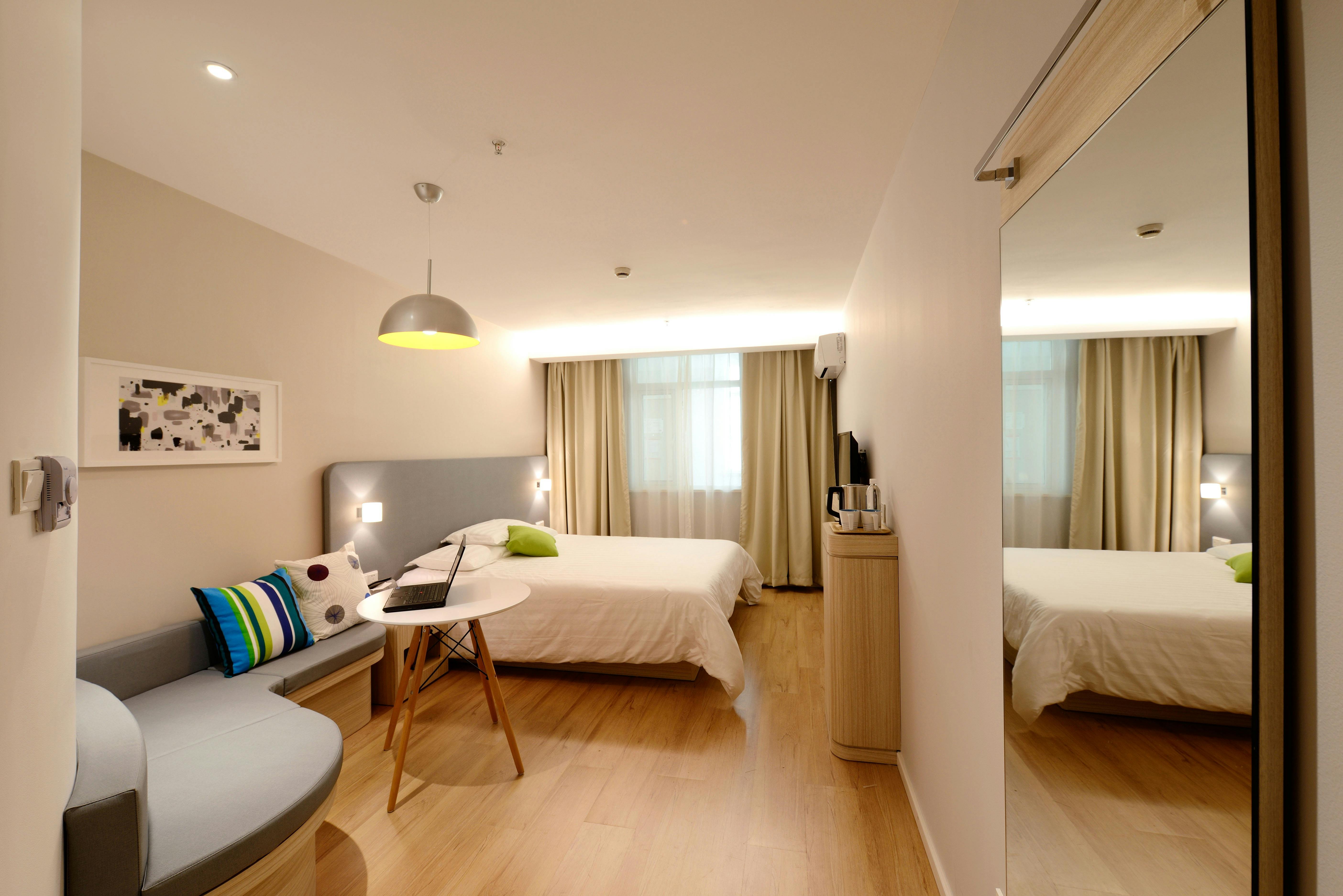Quarto moderno com cama de casal, iluminação aconchegante, piso de madeira e cortinas claras.