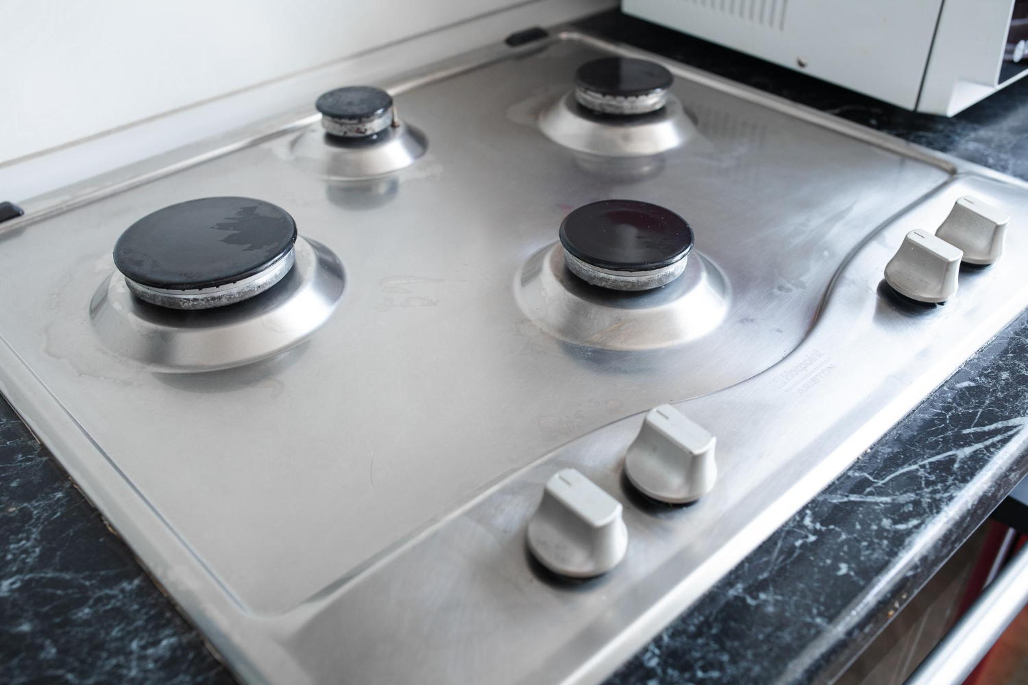 Vista superior de um fogão a gás com quatro bocas e botões de controle, com superfície de inox e queimadores apagados. 