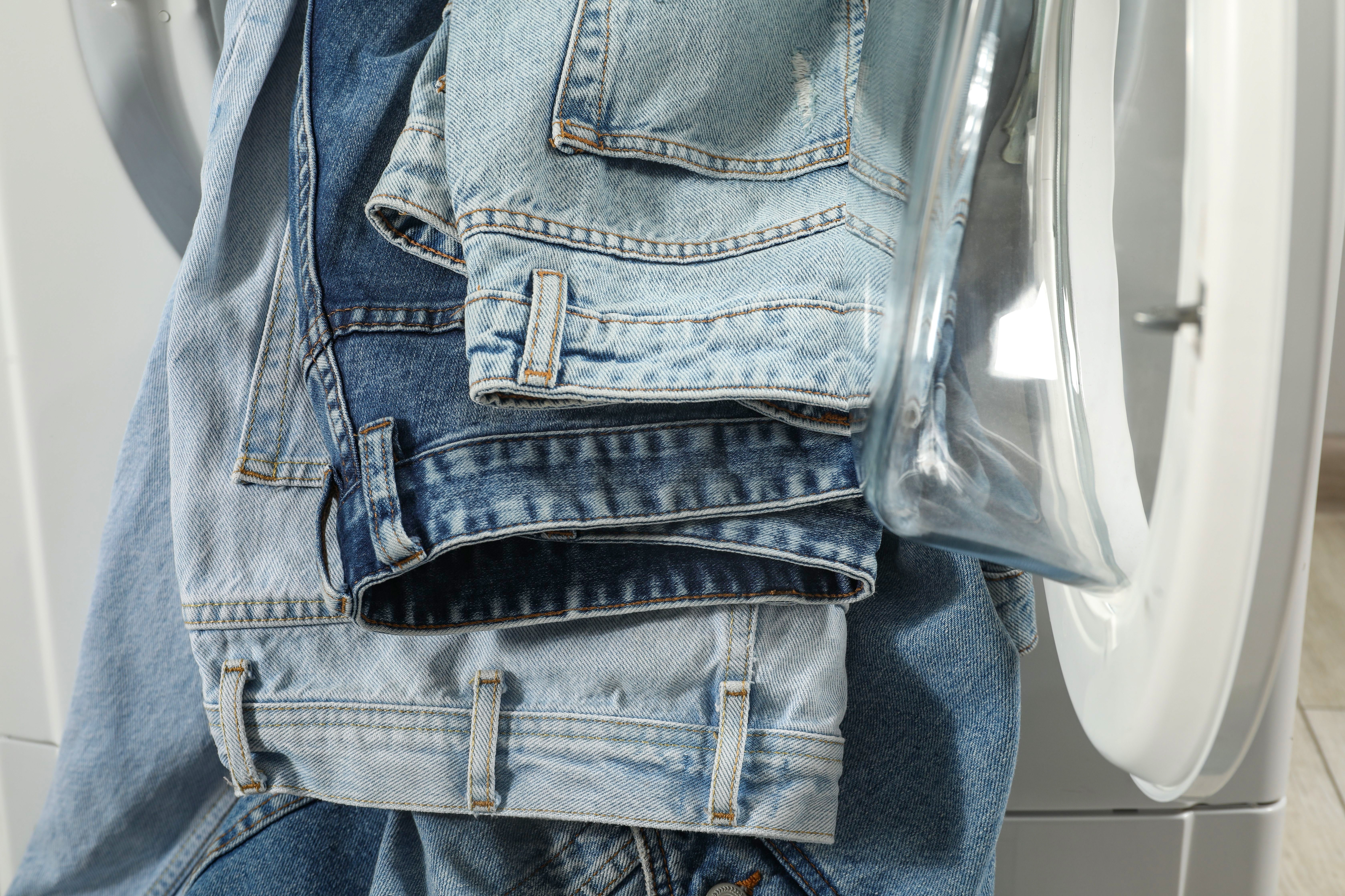 Multiple pairs of jeans hanging out of a washing machine.