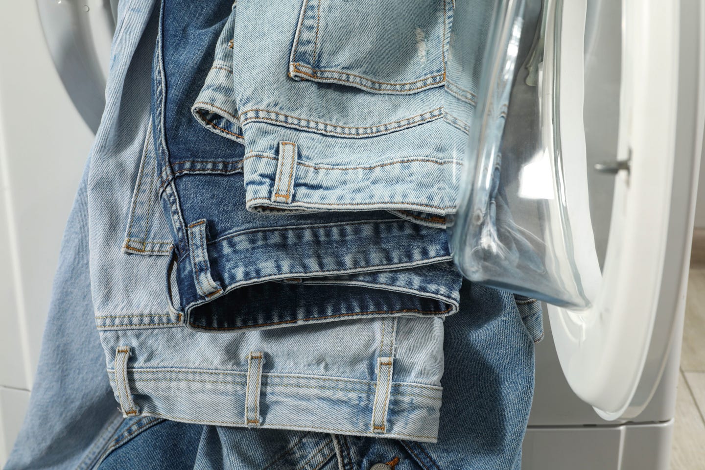 Multiple pairs of jeans hanging out of a washing machine.