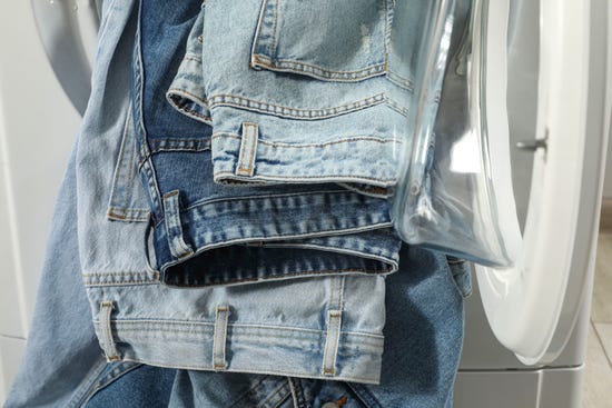 Multiple pairs of jeans hanging out of a washing machine.