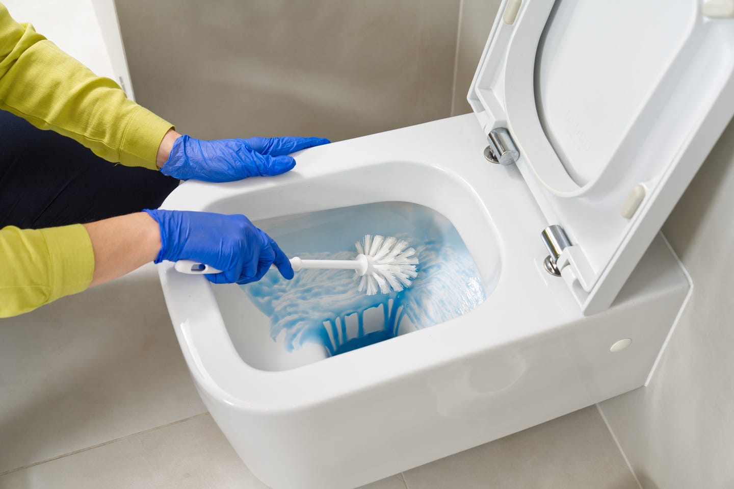A person scrubbing a toilet bowl with a toilet brush and toilet bowl cleaner
