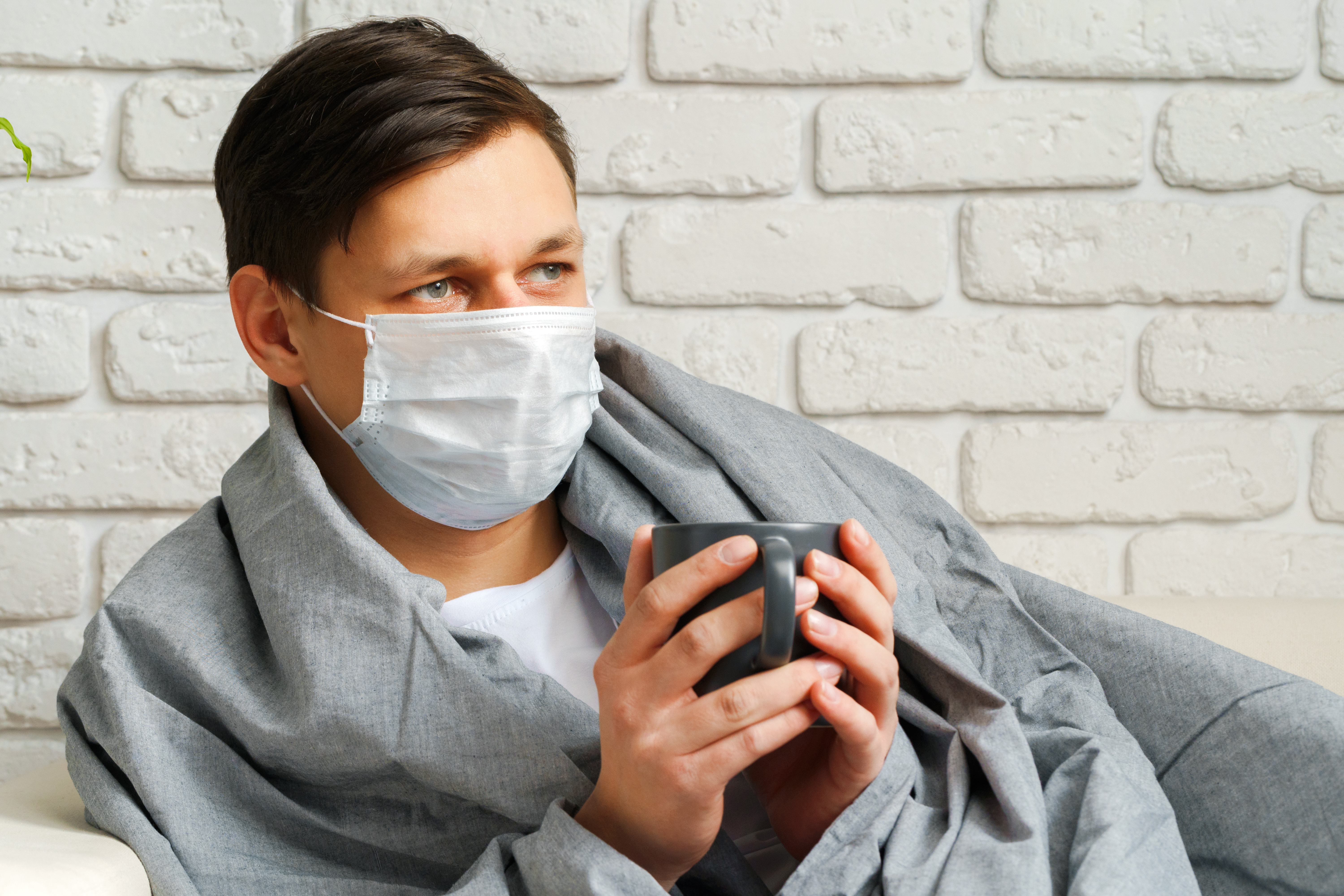 Man wearing face mask sitting and holding a cup.