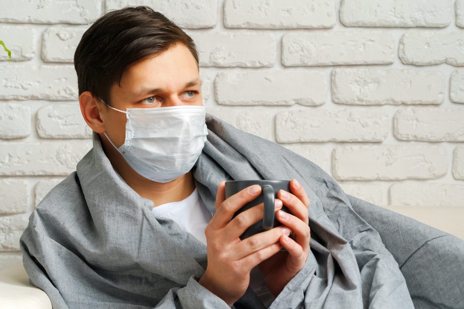 Man wearing face mask sitting and holding a cup.