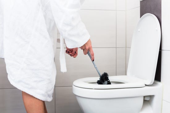 Woman using a toilet brush to clean a toilet bowl.