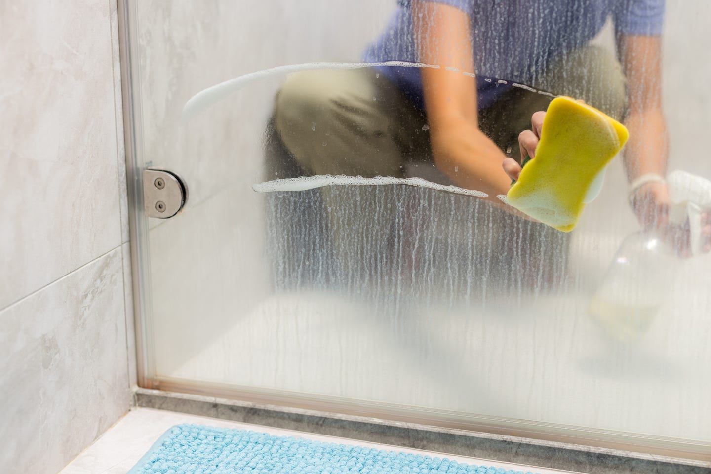 A hand using a sponge to clean the glass of windows in a bathroom