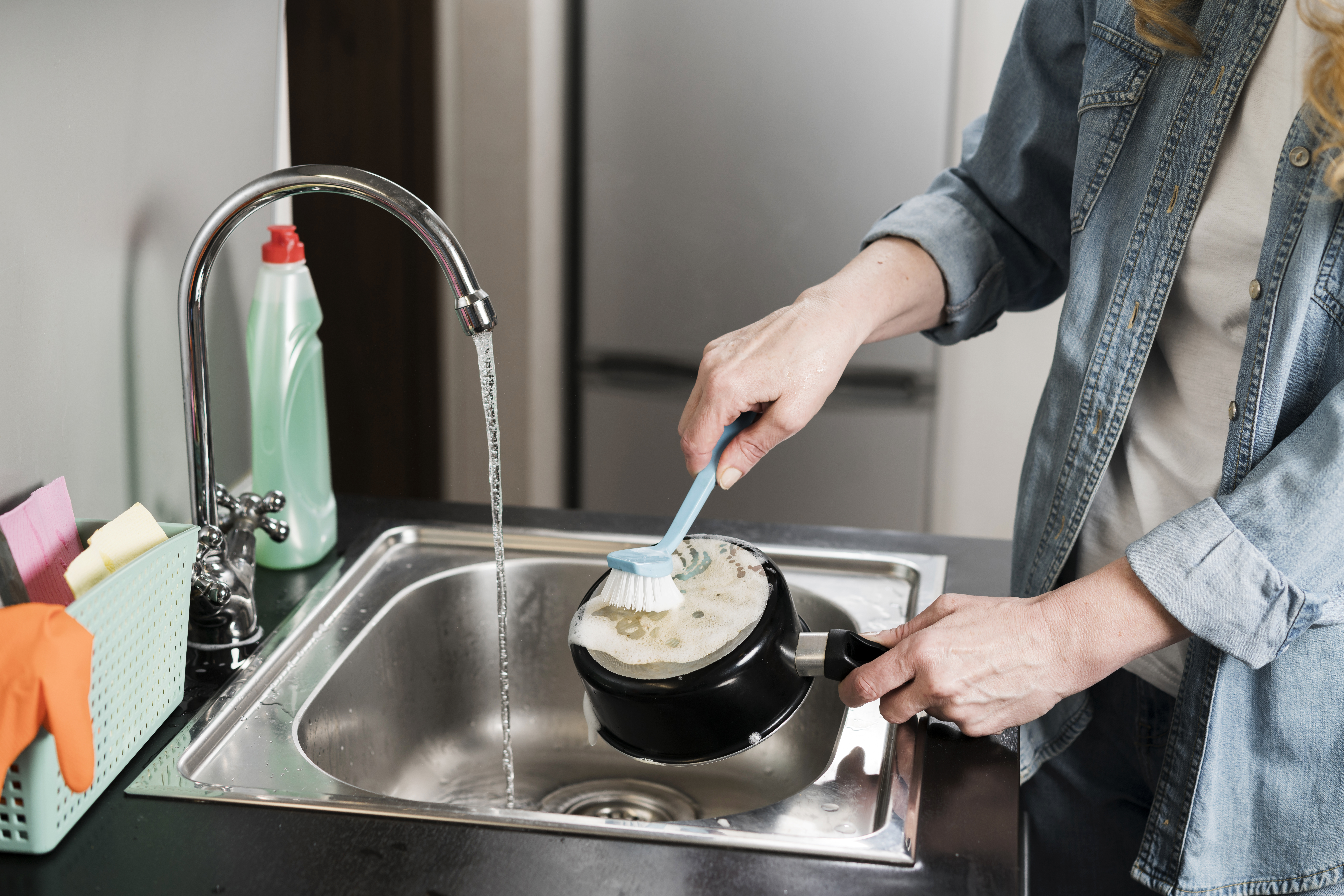 A person is scrubbing a pot with a sponge under a running faucet. 