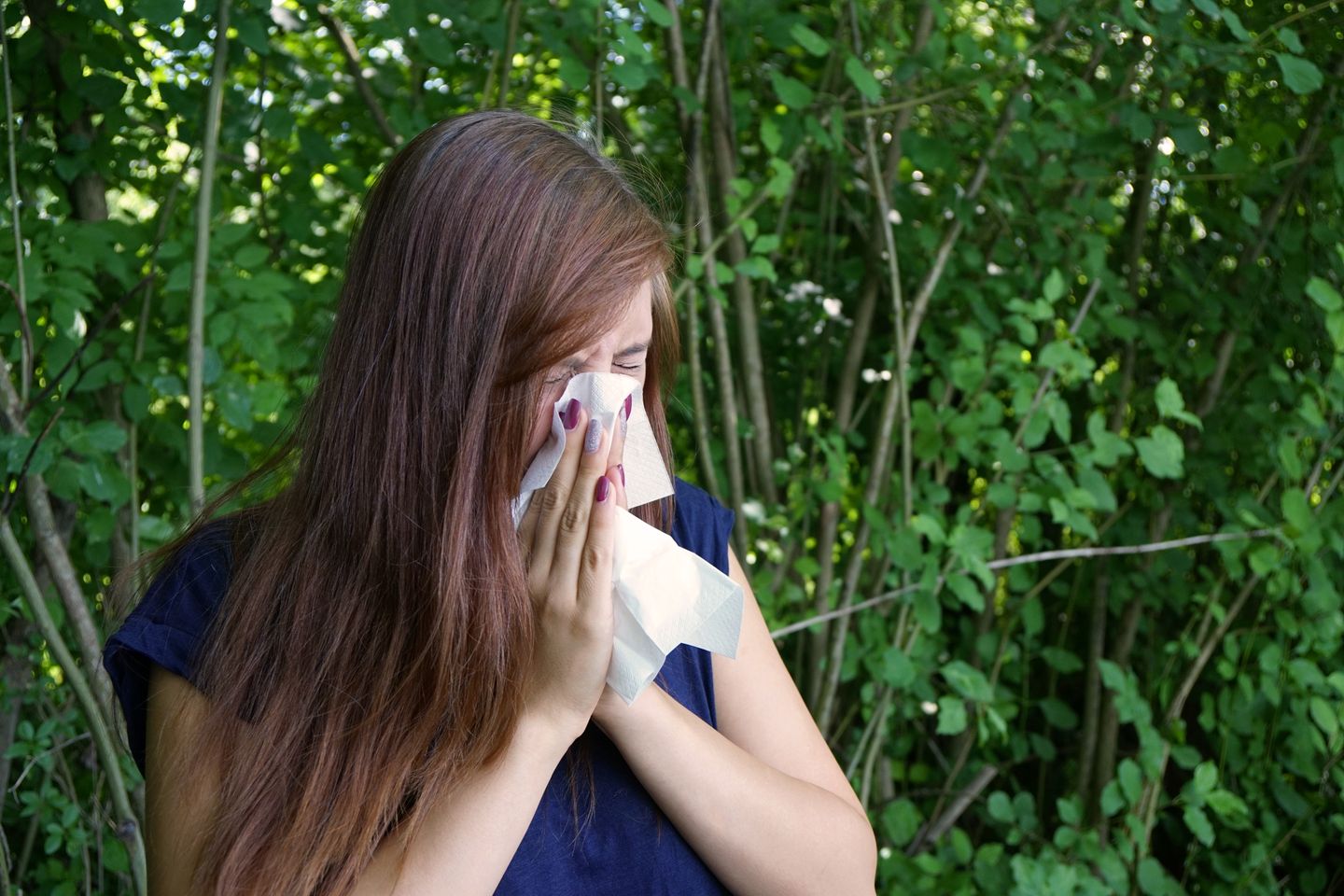 A woman blowing her nose into a tissue outdoors
