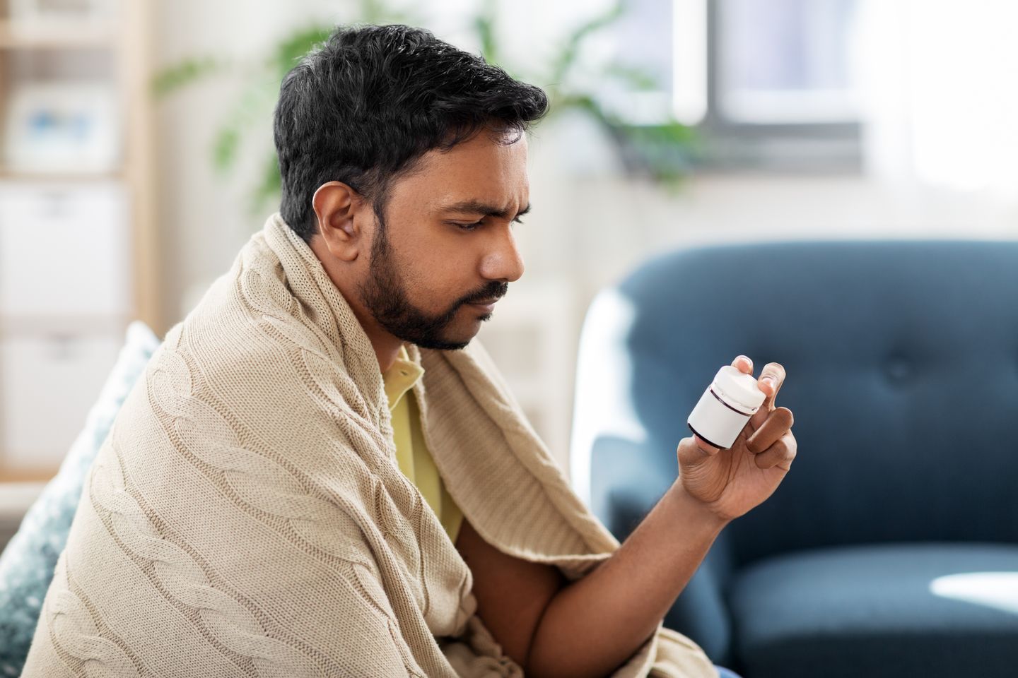 A man wrapped in a blanket, examining a bottle of medicine.