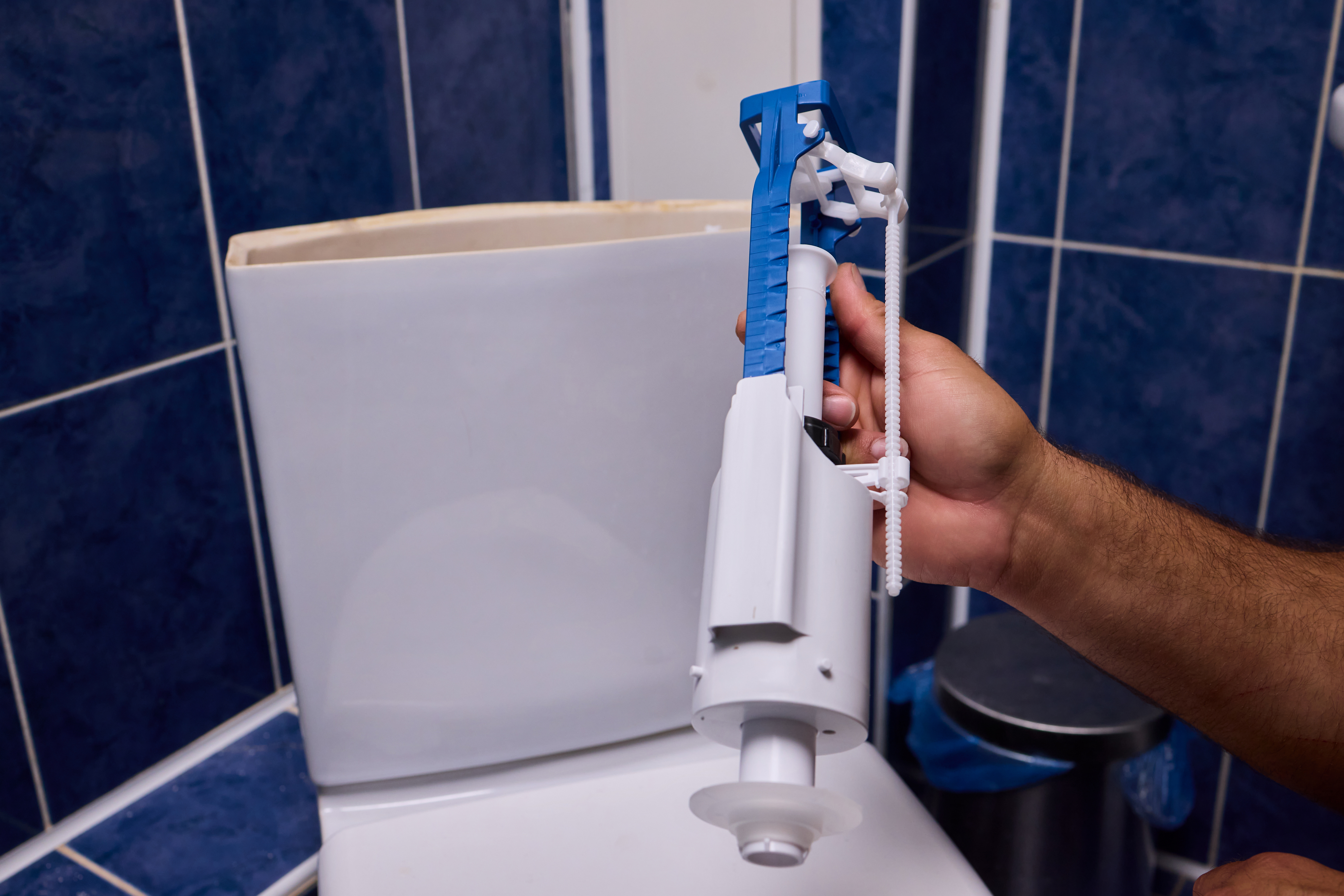 Person holding a toilet valve in front of a toilet.