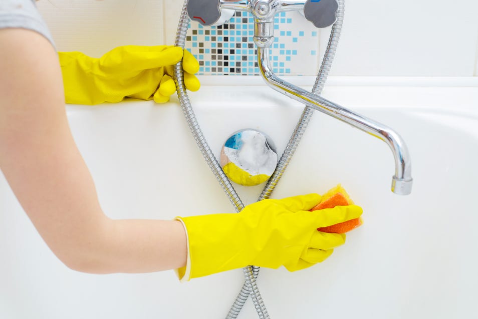 Person in yellow gloves cleaning bathtub with a sponge