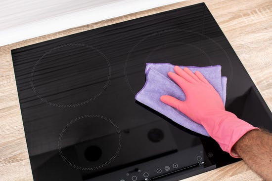 A hand in a pink rubber glove cleaning an induction stove top with a cloth