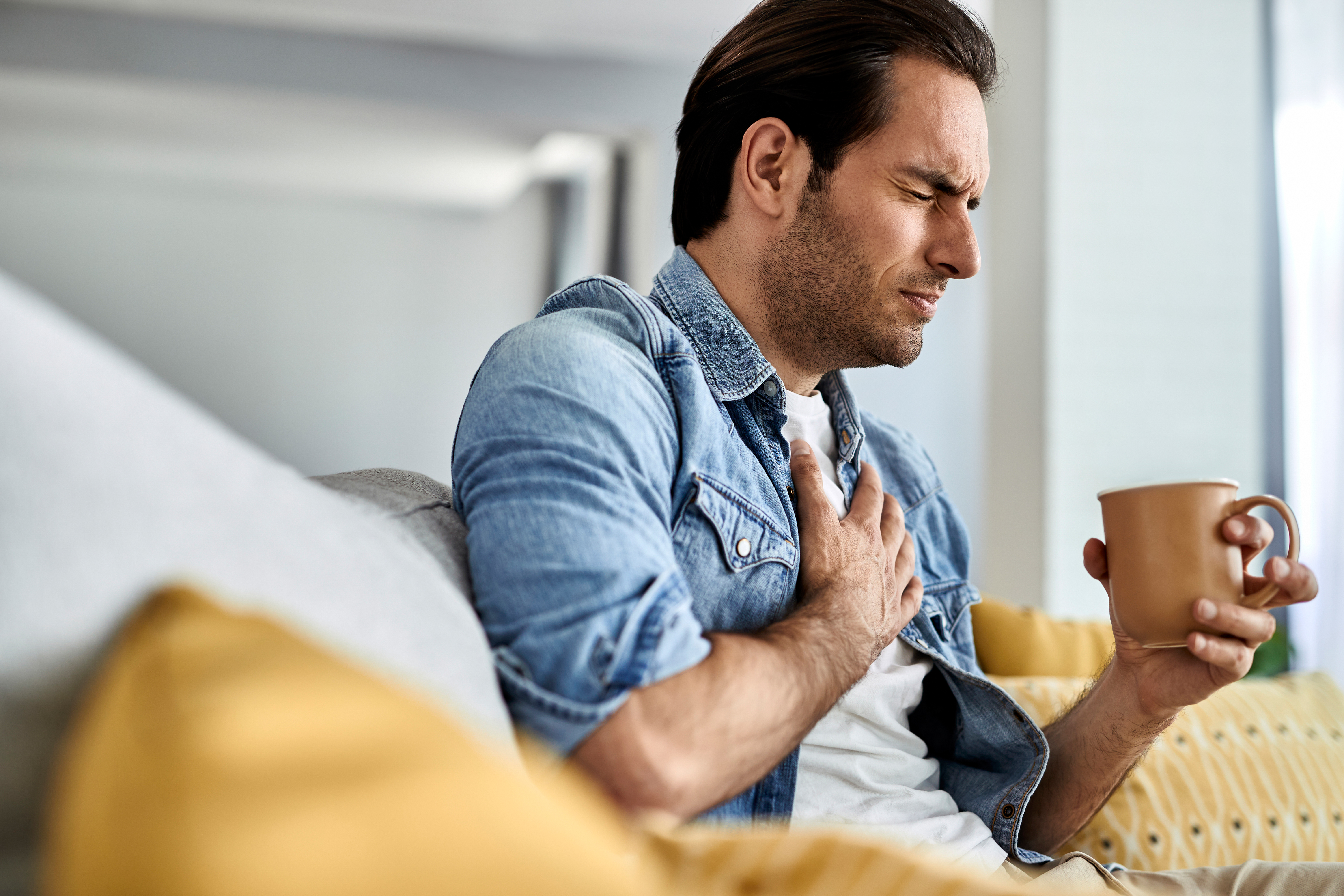 Man holding his chest in pain while drinking tea in the living room.