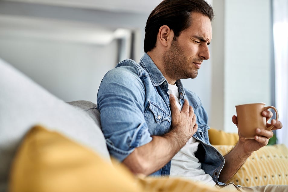 Man holding his chest in pain while drinking tea in the living room.