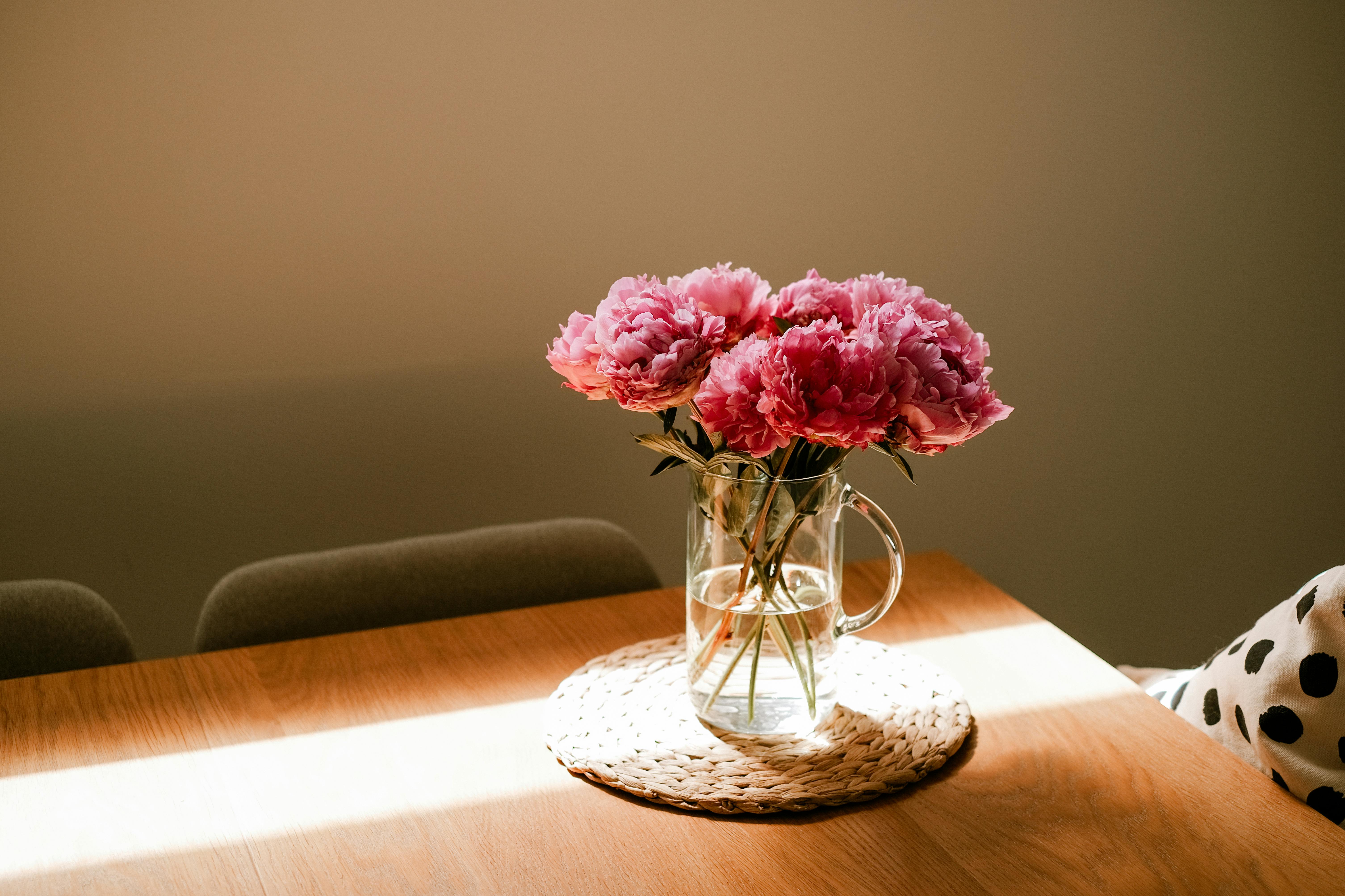 Vaso de vidro com flores rosas sobre mesa iluminada pela luz natural.