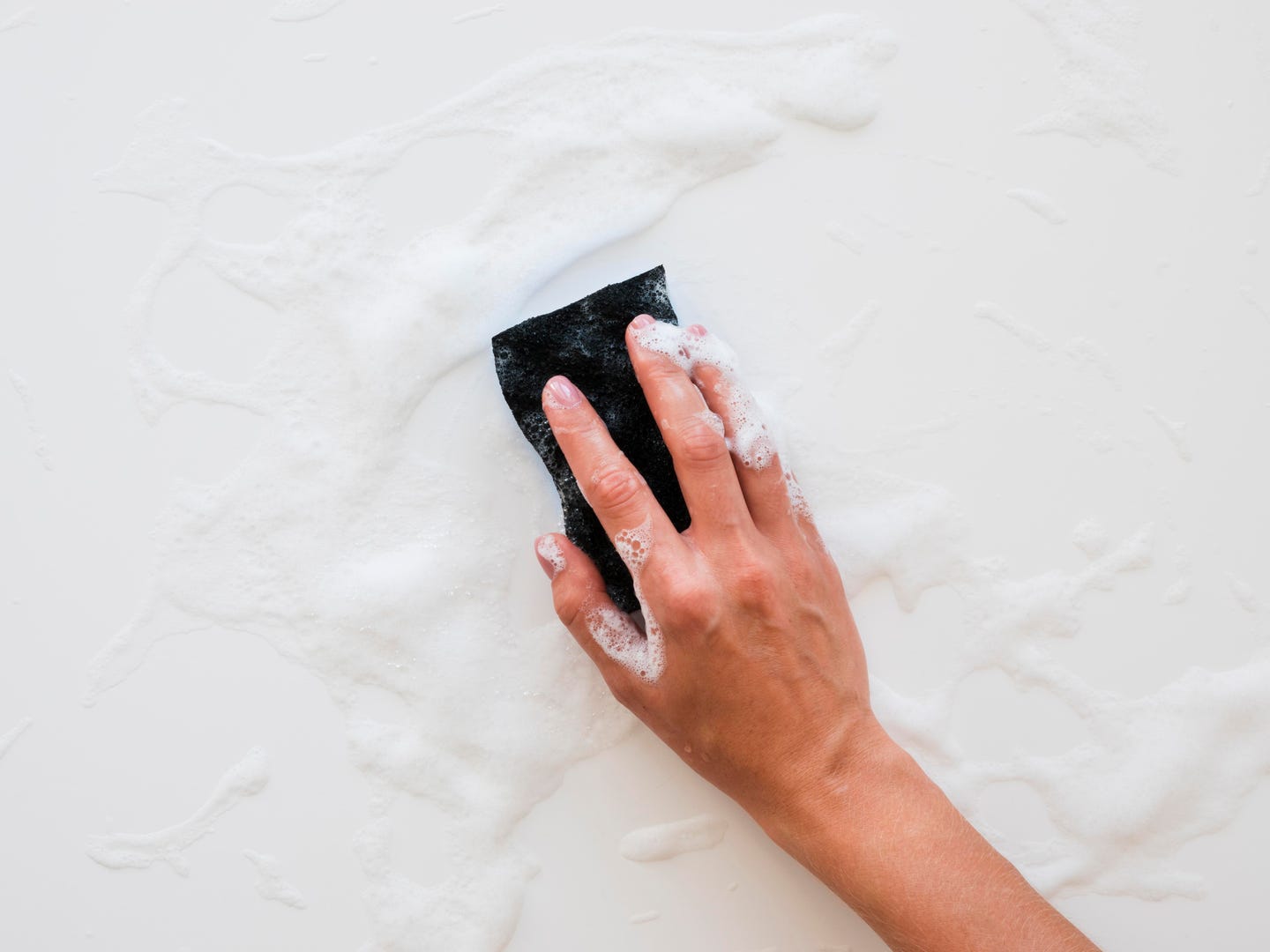 A hand cleaning a surface with a sponge and foam