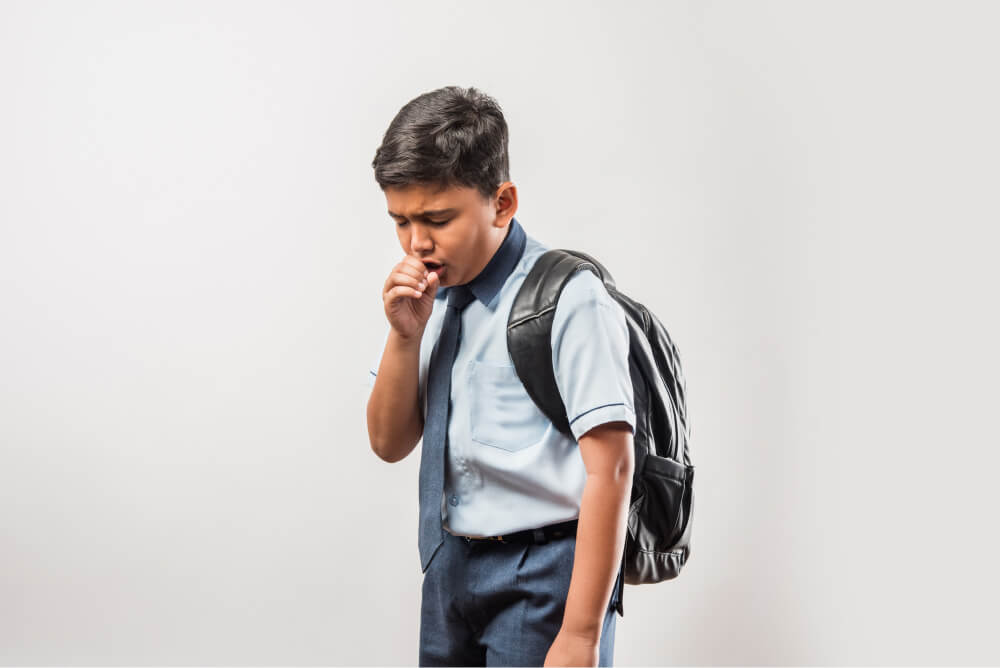 Niño tosiendo con uniforme escolar azul y mochila negra