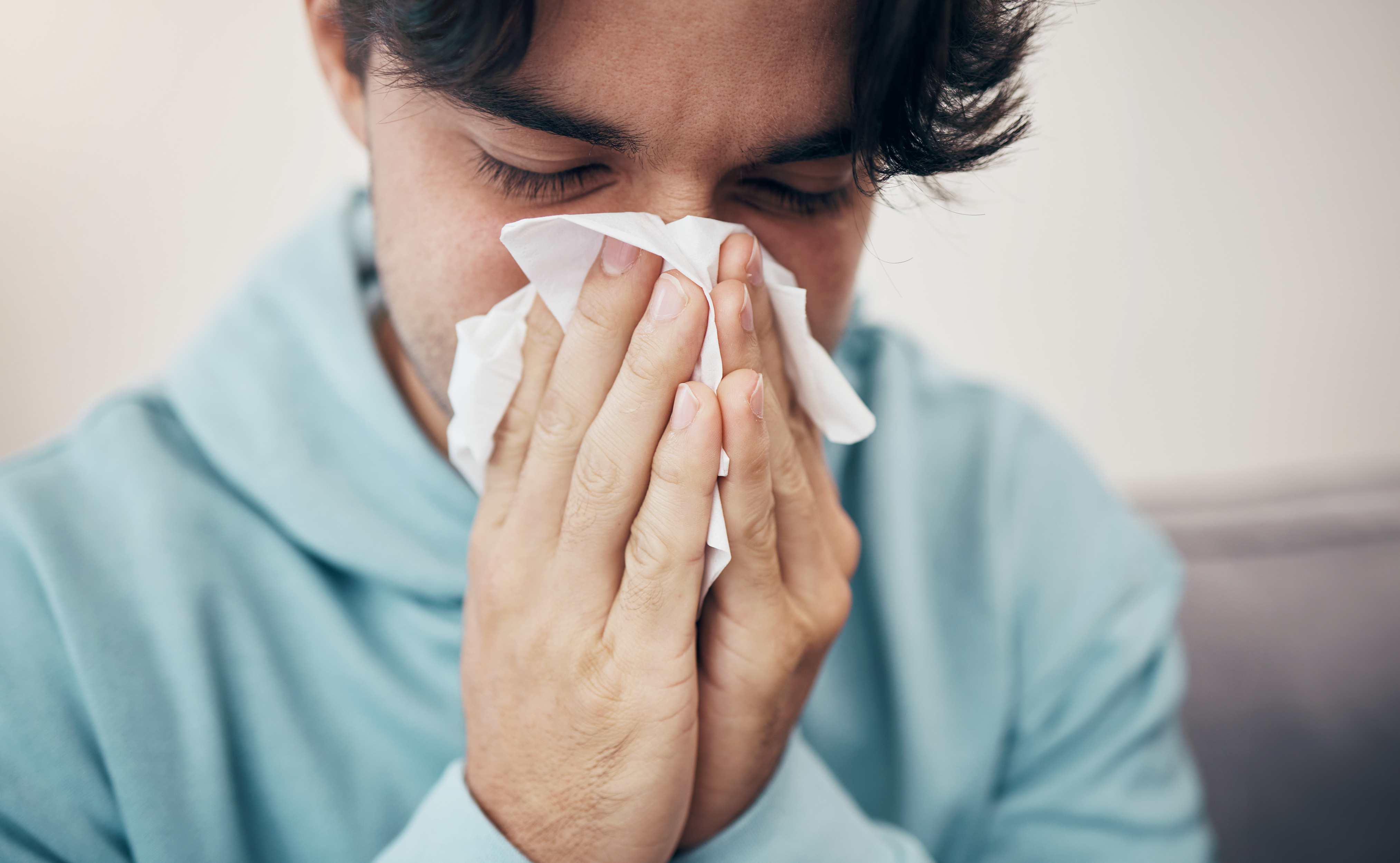 A man blowing his nose into a tissue with his eyes closed