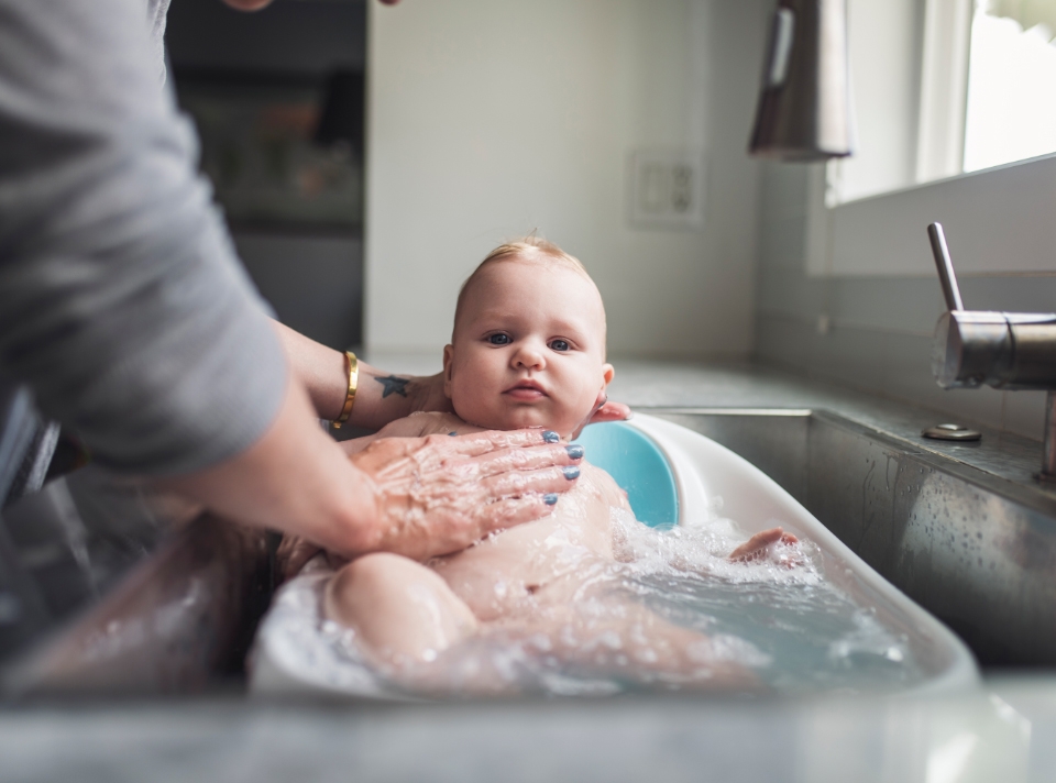 A mother is giving bath to a infant in a small tub